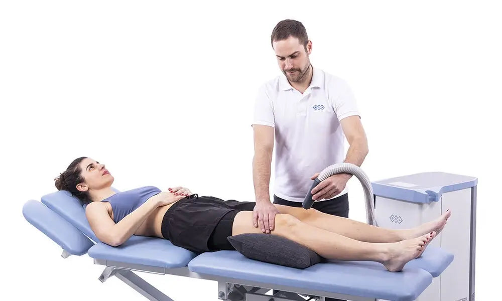 Anwendung des BTL-Kryo durch Therapeuten am Knie einer Frau auf einer Therapieliege