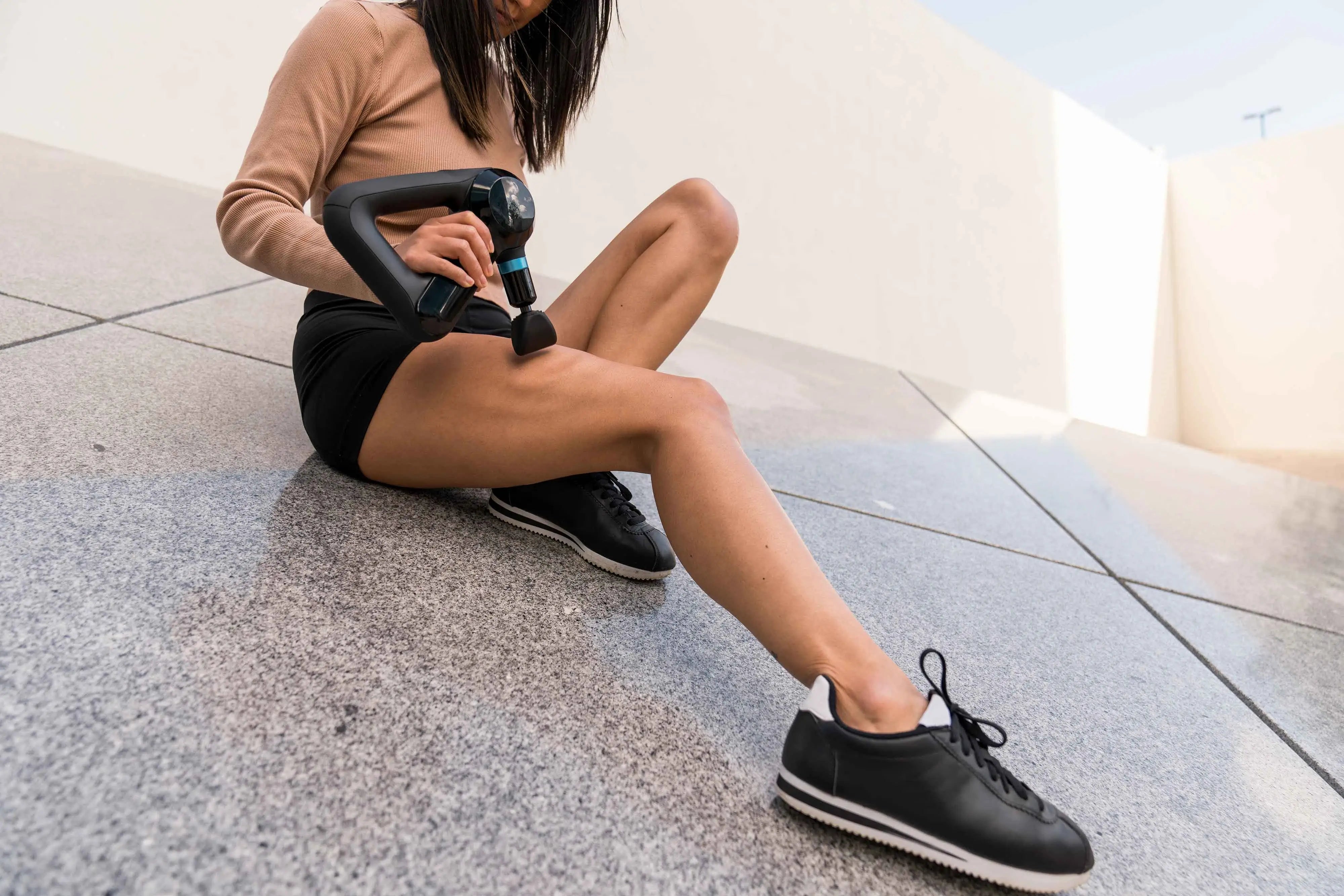 Frau massiert Oberschenkel mit Vibrationsmassagegerät Theragun Elite