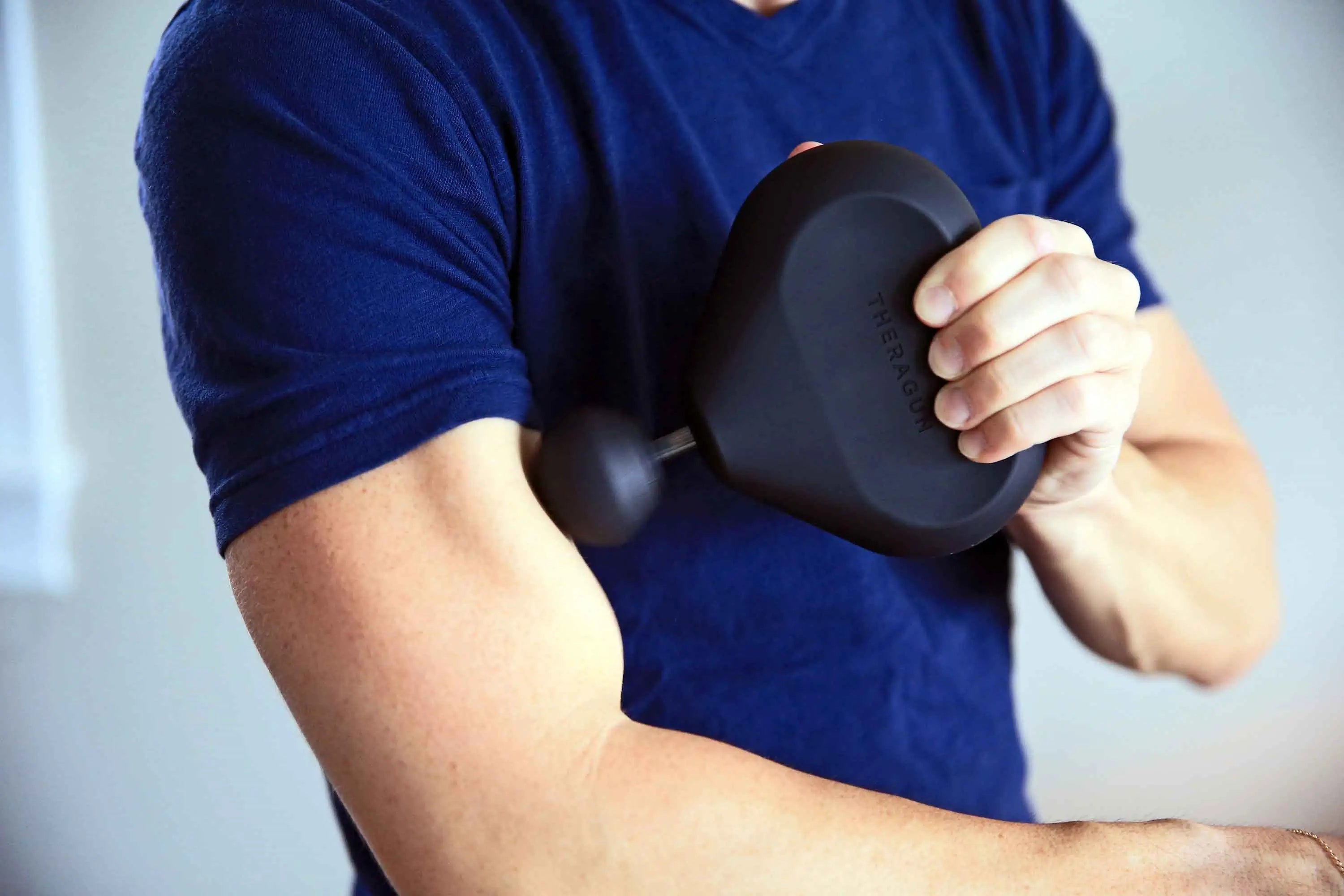 Mann massiert Bizeps mit der Massagepistole Theragun Mini