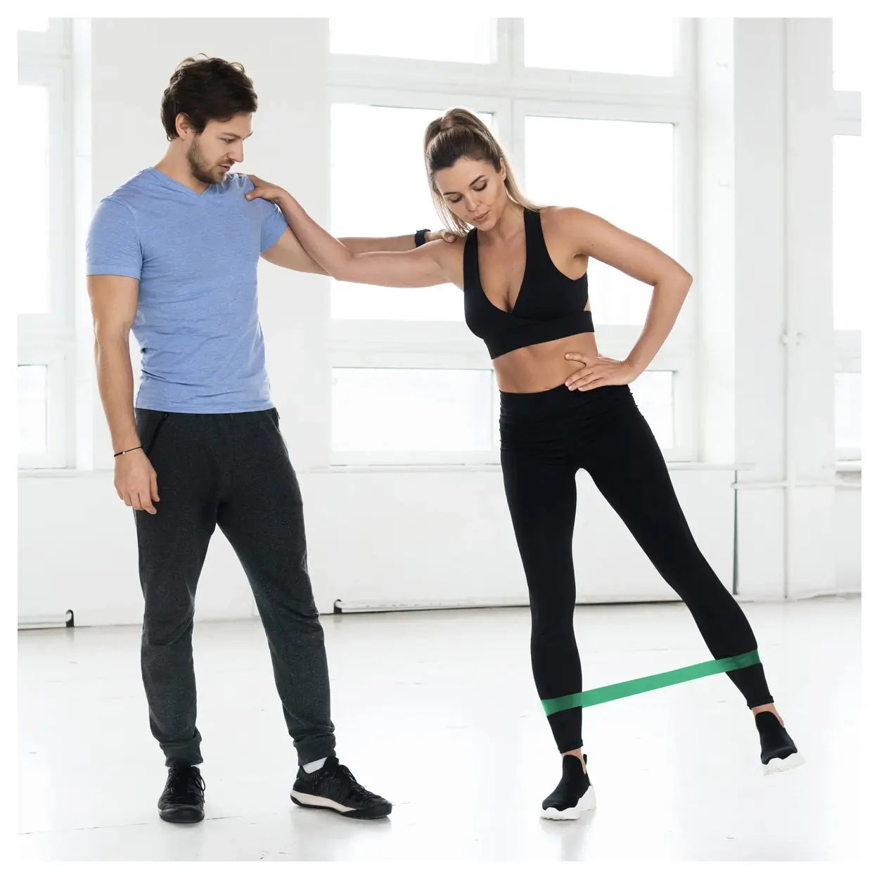 Frau trainiert mit grünem Rubberband Sport-Tec die Hüfte unter Anleitung eines Fitnesstrainers