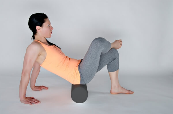 Frau sitzt auf Faszienrolle Black Pearl und stützt Oberkörper mit den Armen auf dem Boden ab