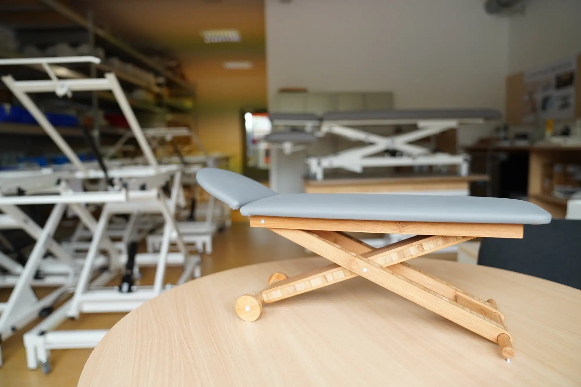 Miniatur Massageliege Vario Nature steht auf rundem Holztisch in Produktionsstätte