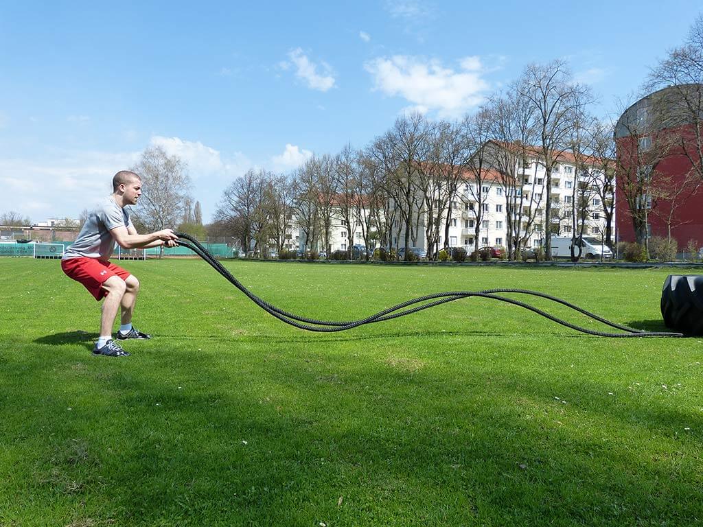Mann trainiert auf Wiese mit Battle Rope Blackthorn 35mm, welche durch Reifen fixiert ist