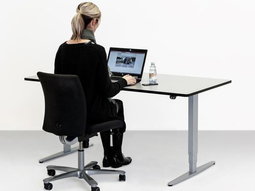 Frau sitzt auf Bürostuhl und arbeitet am Ergo-Schreibtisch Ropox Ergo mit Notebook
